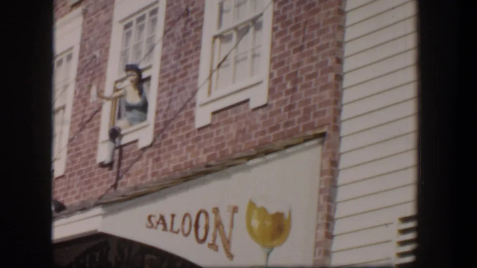 1954 Las Vegas saloon exterior with brick walls, white-trimmed windows, painted signage, and a woman gesturing from an upper window.