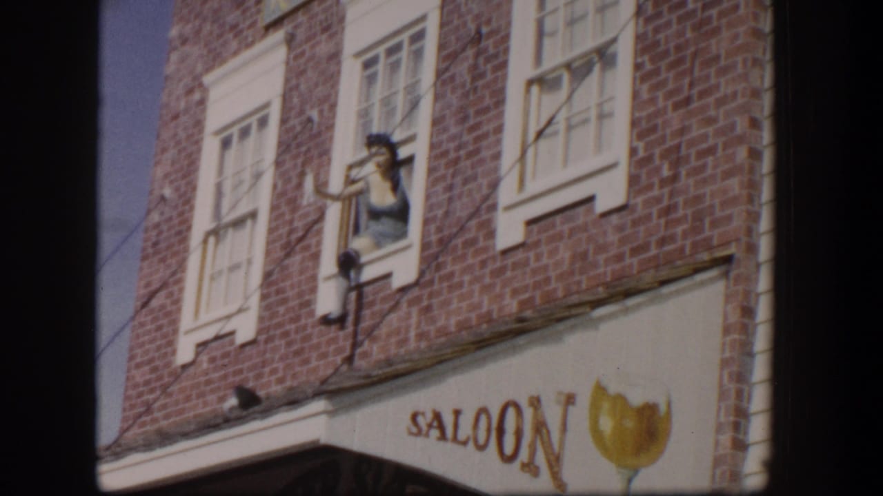 Upper brick facade with saloon sign, beer-glass graphic, and woman waving from a window.