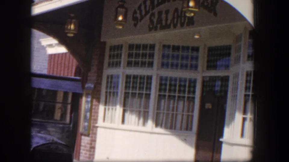 1954 Las Vegas frame with the saloon sign partly visible above large multi-pane windows and a shadowed doorway.