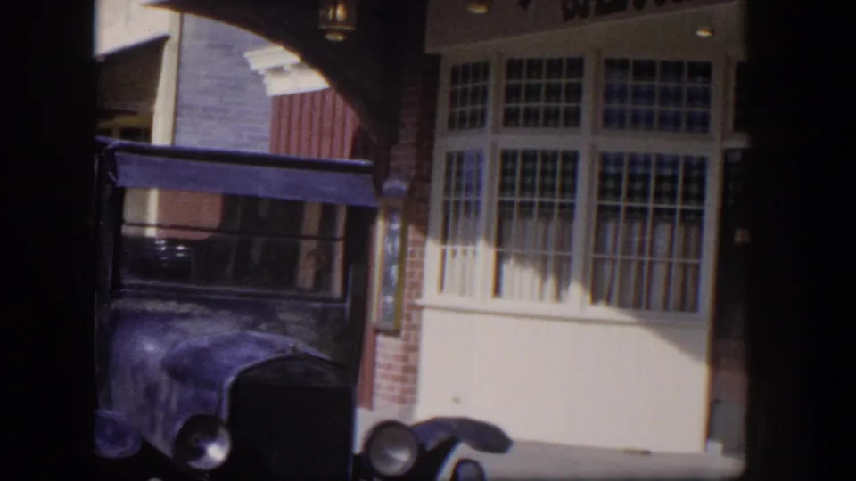 1954 Las Vegas home-movie view of the saloon's lower facade, multi-pane windows, brick edge, and parked older automobile.