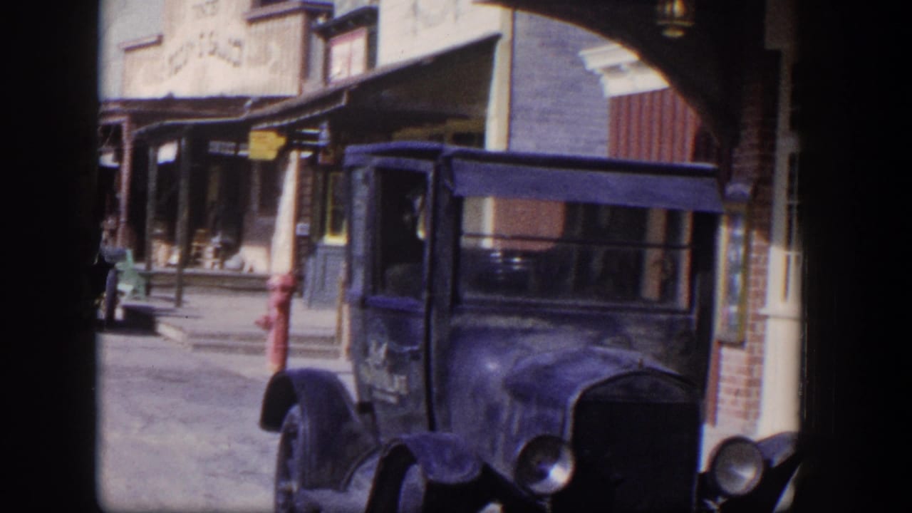 Dark vintage truck parked beside storefronts and a red fire hydrant on a sunny street.