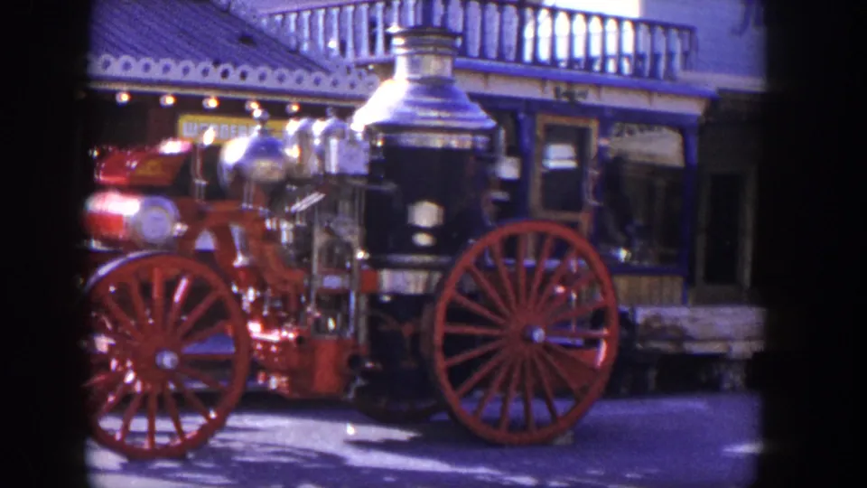 1954 Las Vegas home-movie frame showing an ornate steam fire engine with red spoked wheels beside a storefront facade.