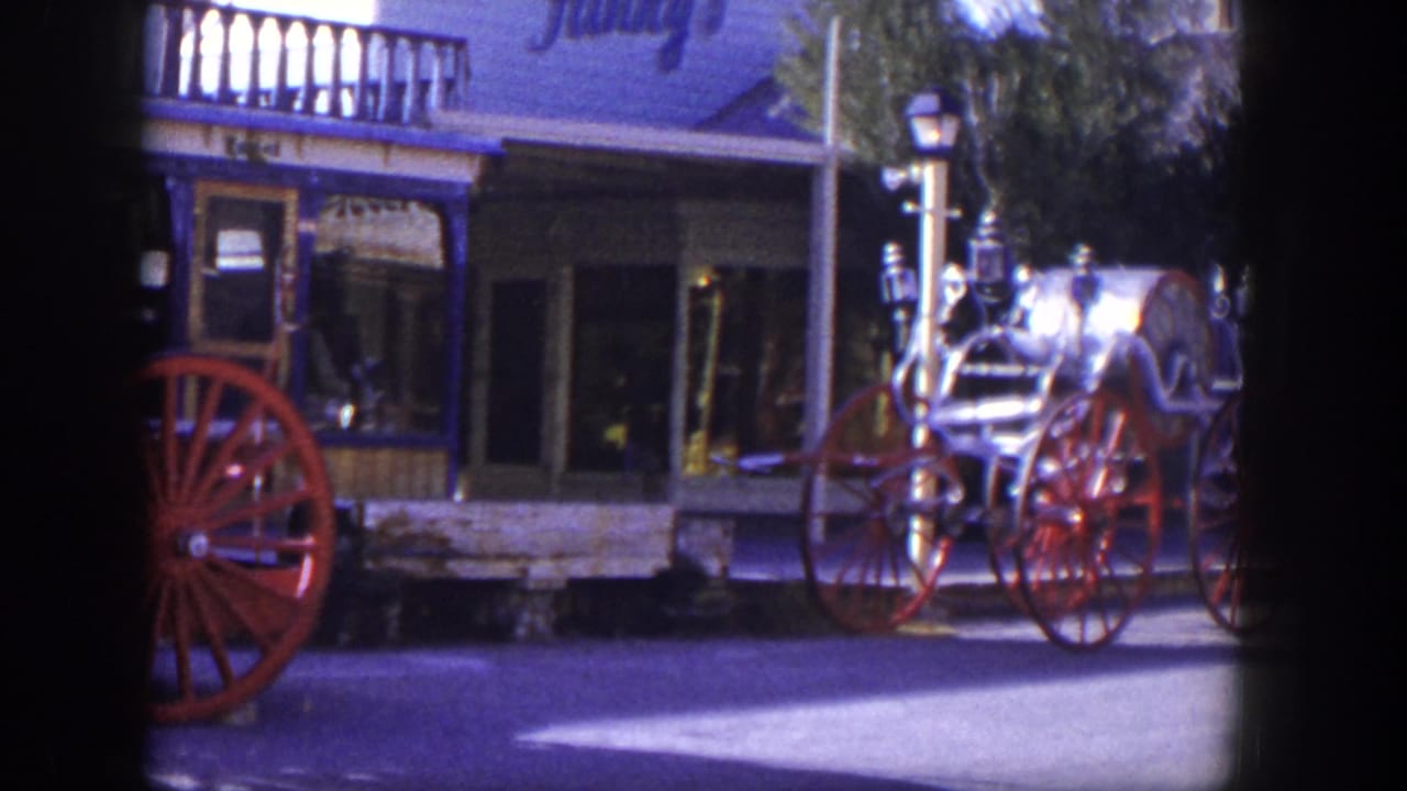 1954 Las Vegas 8mm frame showing a vintage fire engine with red spoked wheels beside a storefront-lined street.