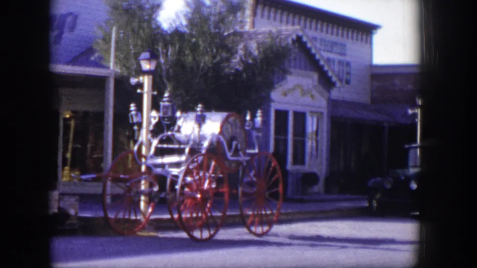 Late frame of the 1954 Las Vegas shot showing the red-wheeled fire engine near storefronts and a partial dark vehicle at right.