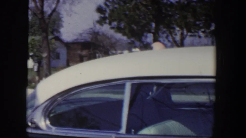 Side view of the 1954 two-tone car with rounded roofline and residential houses in the background.