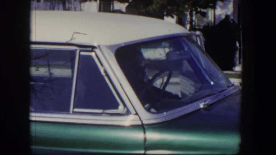 Home-movie frame from 1954 Las Vegas showing the green sedan door, white roof, steering wheel, and surrounding daylight street scene.