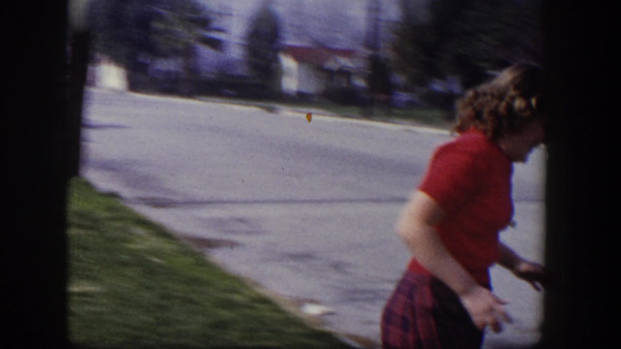 Young woman in a red sweater walking beside a sidewalk near a lawn.
