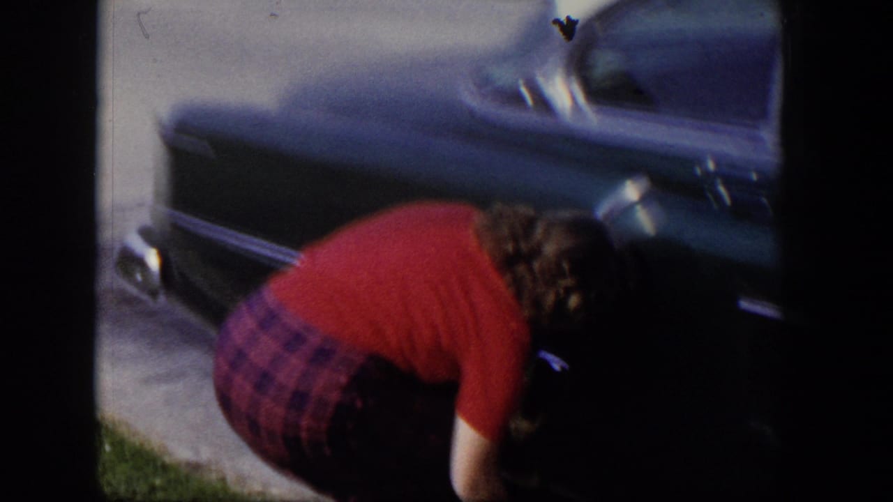 Young woman bending near the front of a parked dark car.