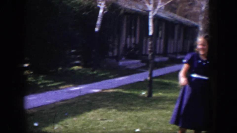 Young woman stands on the grass near a sidewalk in 1954 Las Vegas, holding or preparing to throw a ball in a casual home-movie moment.