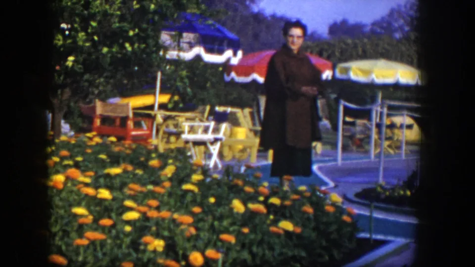 1954 Las Vegas home-movie frame of a woman posing beside marigold-like flowers, patio seating, and colorful umbrellas.