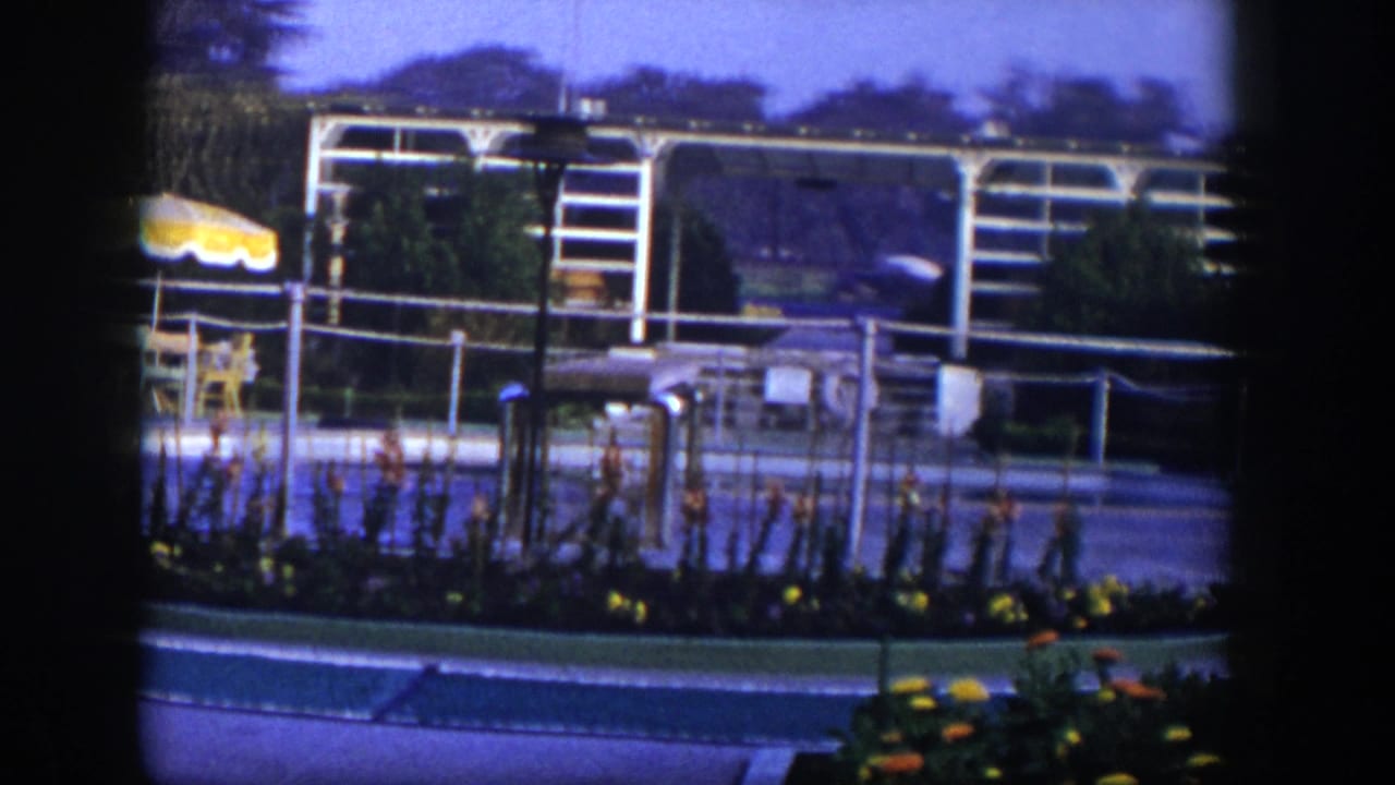 1954 Las Vegas home-movie frame showing a landscaped paved area with white metal framework, railings, flowers, and outdoor seating details.