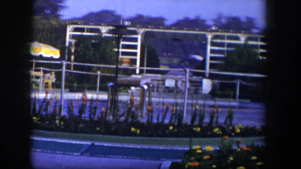 1954 Las Vegas home-movie frame showing a landscaped paved area with white metal framework, railings, flowers, and outdoor seating details.