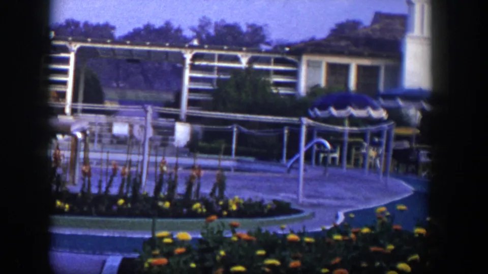 1954 Las Vegas home-movie view of a landscaped outdoor area with a low building, blue umbrella, chairs, railings, and white framework.