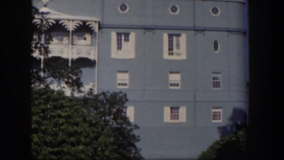 1954 Las Vegas home-movie view of a blue hotel exterior with white balcony trim, small windows, and dense trees in the foreground.