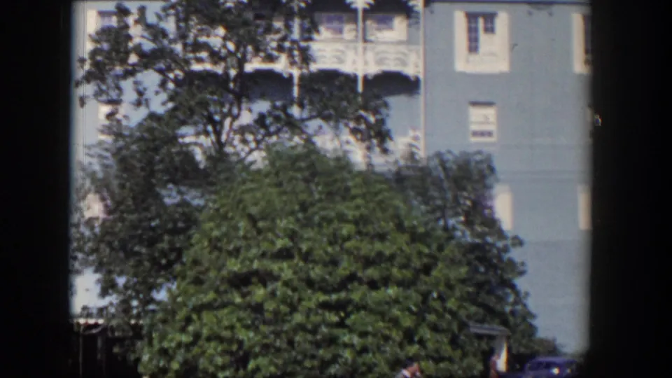 1954 Las Vegas frame with leafy trees in front of a light-blue hotel facade and ornate white balcony details.
