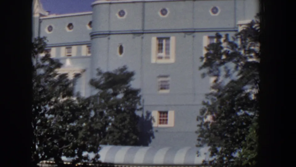 1954 Las Vegas frame showing the rounded corner of a light-blue hotel, circular windows, trees, and a striped awning.