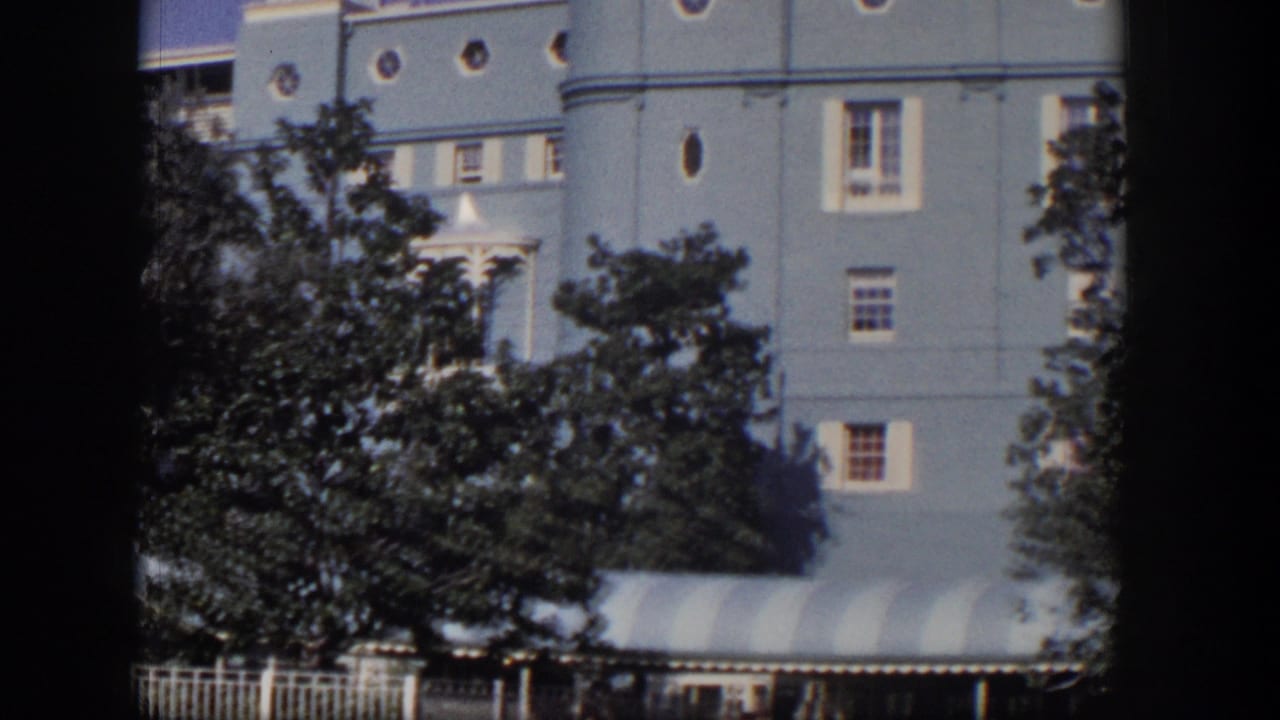 1954 Las Vegas home-movie view of a large light-blue mansion facade with round windows, trees, fence, and striped awning.