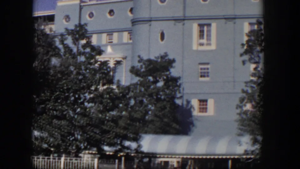 1954 Las Vegas home-movie view of a large light-blue mansion facade with round windows, trees, fence, and striped awning.