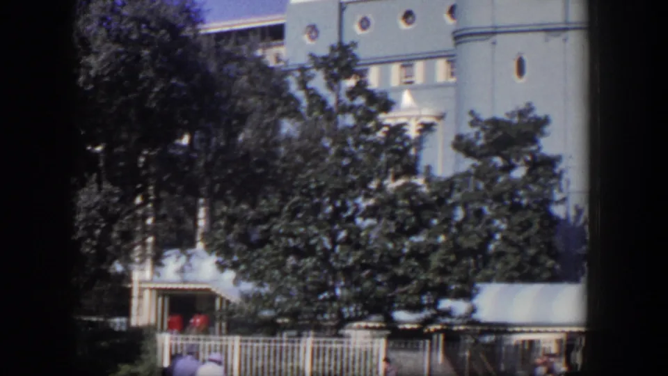 A Las Vegas mansion or hotel-like exterior appears behind trees, with a striped awning, white fence, and small figures near the entrance.