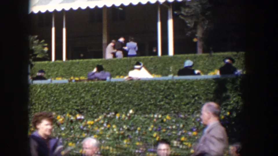 1954 Las Vegas public scene with formally dressed adults, benches, hedges, flowers, and passing pedestrians.