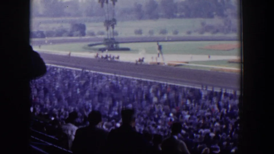 Grandstand view of a Las Vegas horse race, with dark spectator silhouettes in front of a crowded racetrack and green infield.