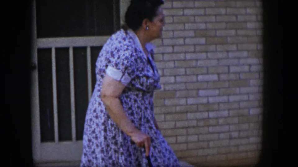 Profile view of the older woman with a walking stick beside a brick entrance, from 1954 Las Vegas 8mm home-movie footage.