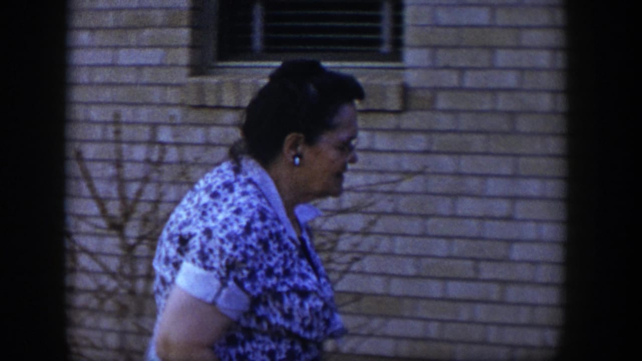 Woman in a patterned dress walking beside a brick wall.