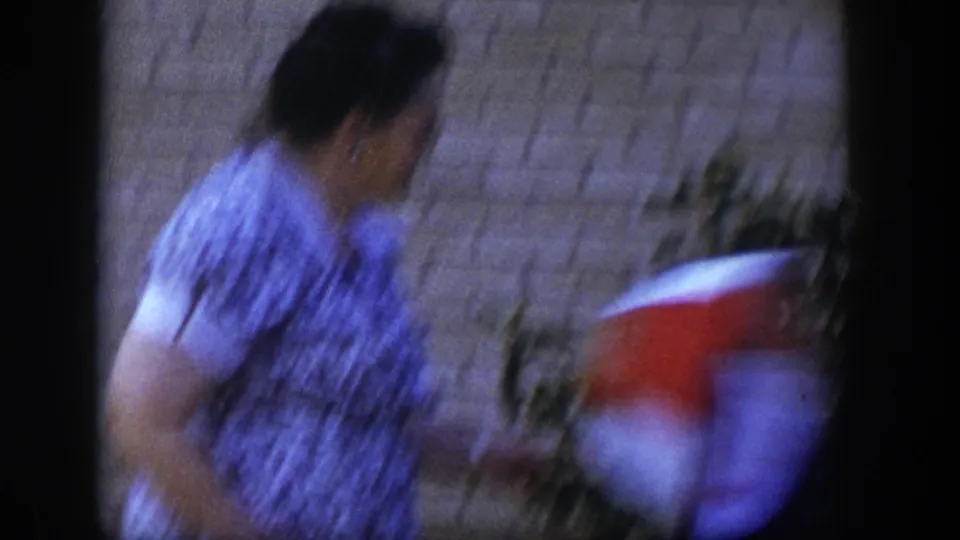 A motion-blurred frame shows the woman passing near the camera, with a red and white object partly visible in the foreground.