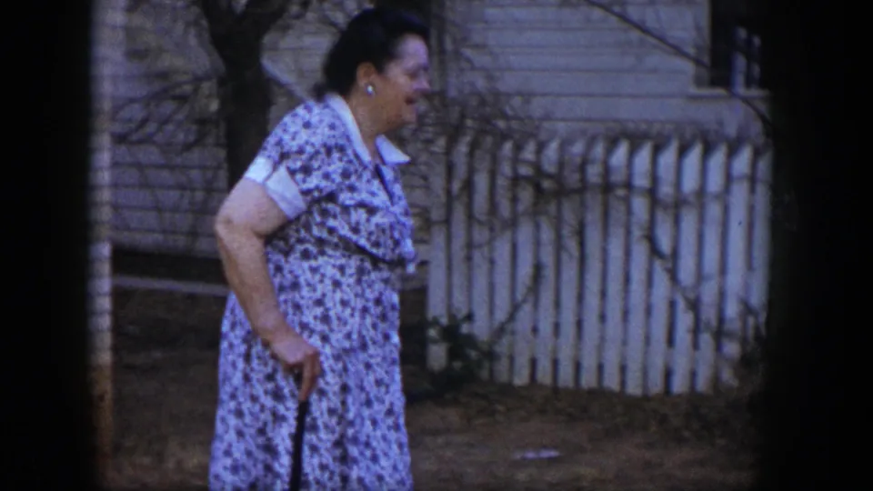 The woman walks along the exterior area near a white picket fence, brick wall, and sparse garden plantings in Las Vegas.