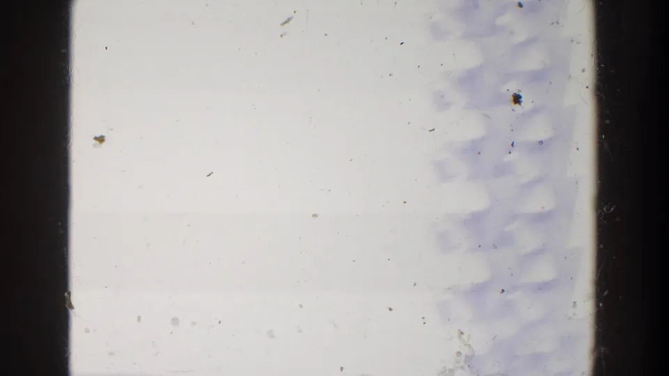 Overexposed 8mm frame with a dark vertical divider, dust, scratches, and faint structures from the reported fairground scene.