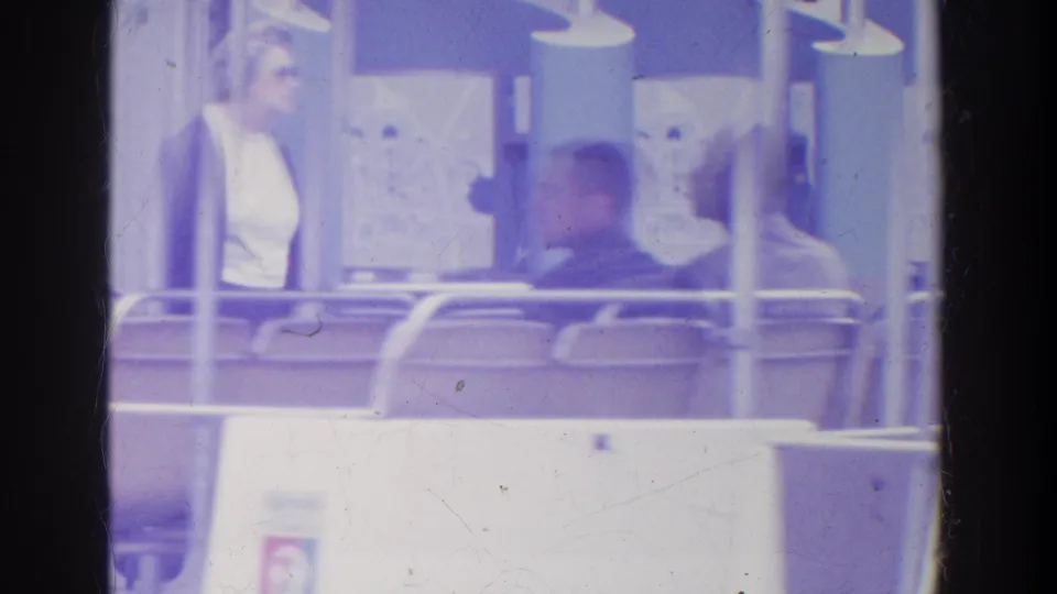A woman stands or turns near the left side while other adults sit in an open tram car framed by railings and support posts.