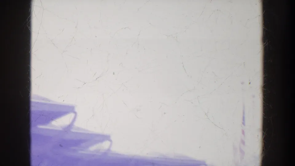 Washed-out 8mm frame showing a partial roofline or structure at lower left with dark film borders and surface wear.