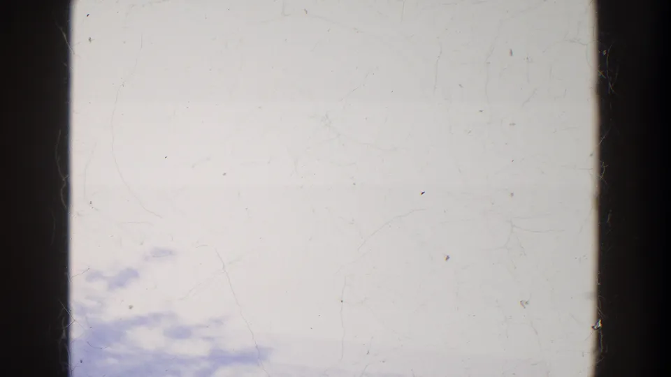 Purple-tinted 8mm frame with faint treeline shadows, pale sky, dark gate edge, and visible dust and scratches.