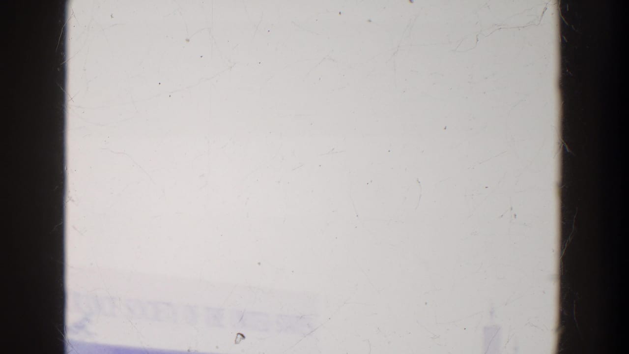 Faint fairground lettering and pale architectural forms appear through an overexposed 8mm frame with dark vertical edges.