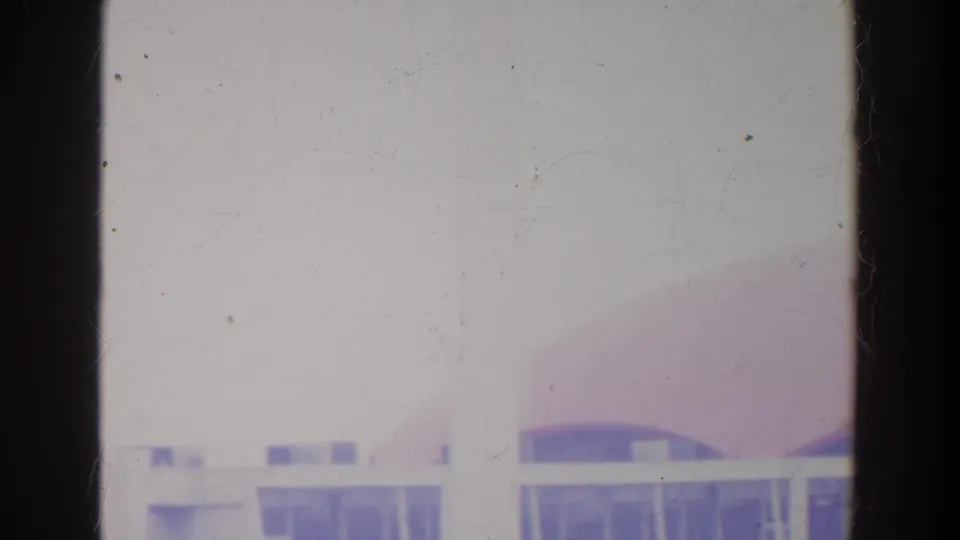 A low, white modernist pavilion with glass window bands sits before a soft pink-purple dome in faded 8mm color.