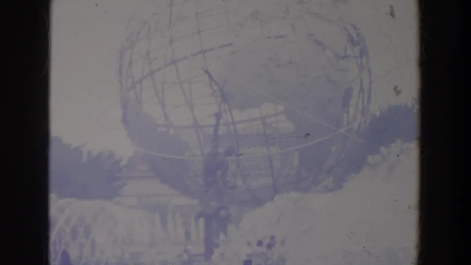 Soft 8mm view of the Unisphere, fountain spray, nearby visitors, trees, and fairground structures in an aged color cast.