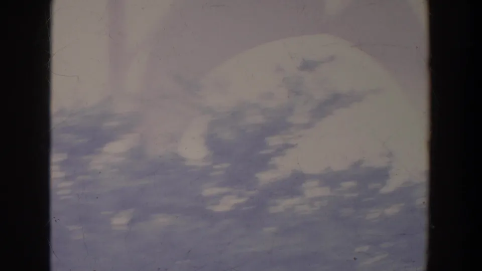 Faded 8mm frame showing bright sky, blurred tree canopy, and dark film gate edges at the start of the clip.
