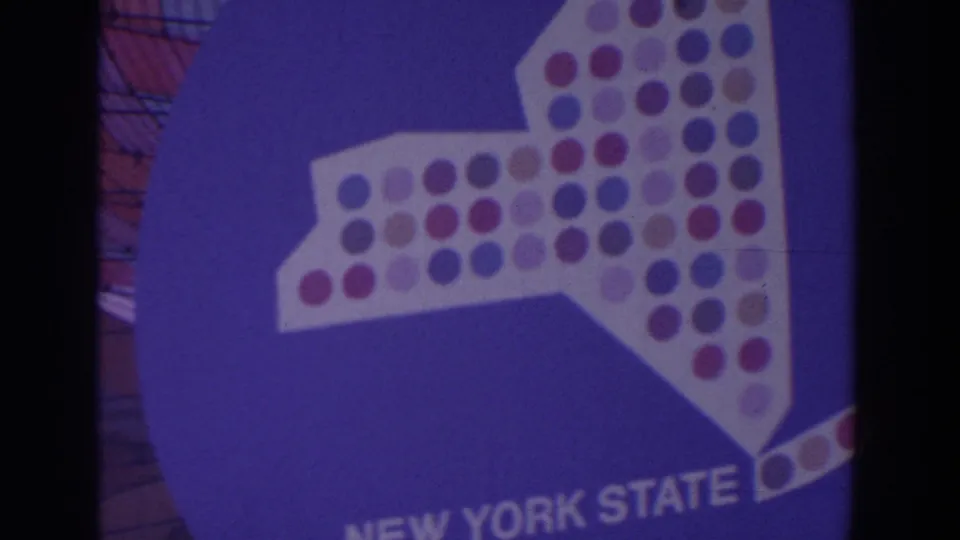 Blue 1964 World's Fair display sign with a white New York State shape, colored dot pattern, and partial NEW YORK STATE lettering.