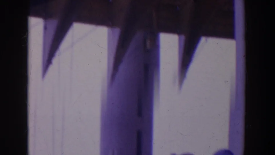 Soft 8mm frame showing the edge of the blue sign and blurred fairground structure below, with strong vertical film borders.