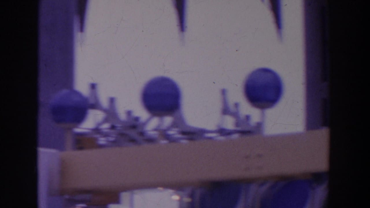Soft 8mm frame of blue spherical structures and small display pieces near a bright fairground building facade.