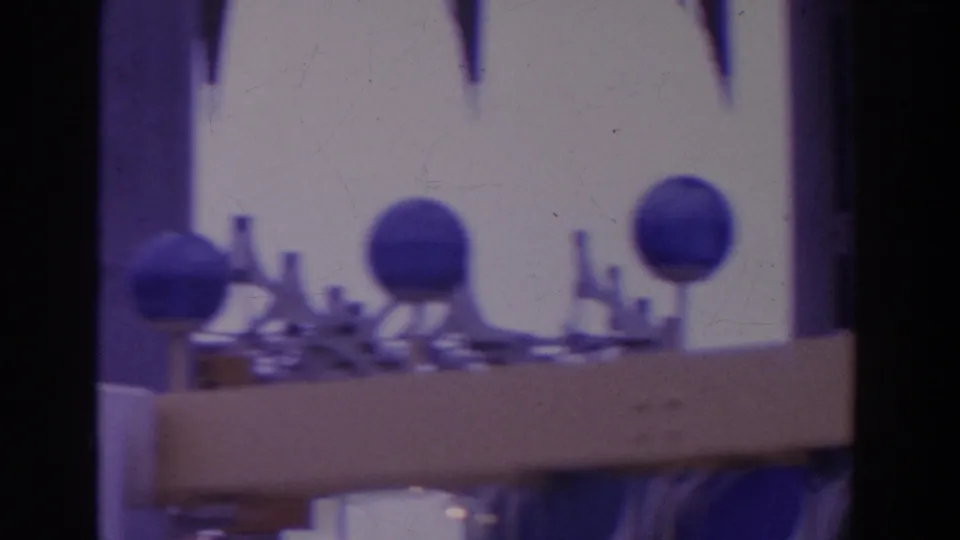 Soft 8mm frame of blue spherical structures and small display pieces near a bright fairground building facade.