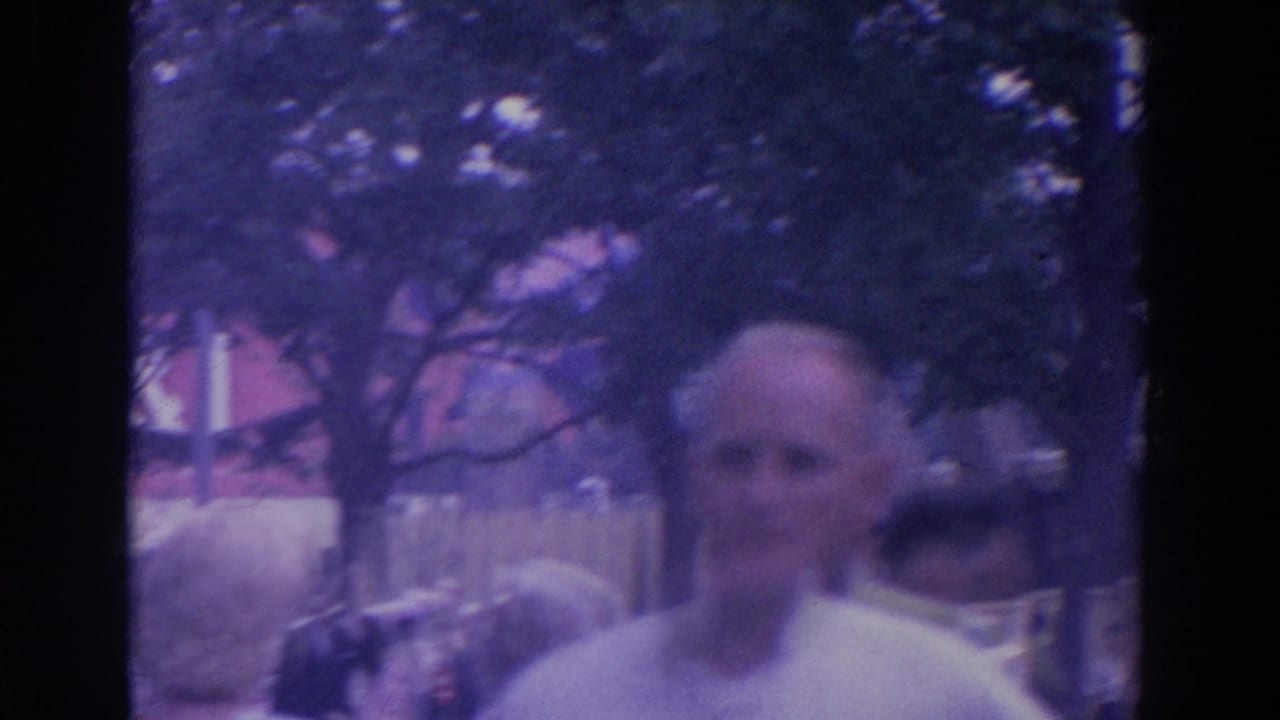 Visitor-shot 8mm frame showing a balding adult man near trees and fairground architecture at the 1964 New York World's Fair.