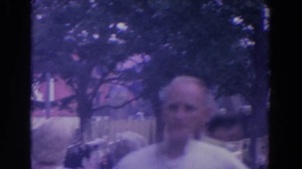 Visitor-shot 8mm frame showing a balding adult man near trees and fairground architecture at the 1964 New York World's Fair.
