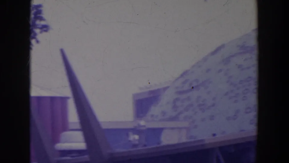Soft 8mm frame showing a pointed form and a large patterned dome-like roof within the 1964 New York World's Fair grounds.