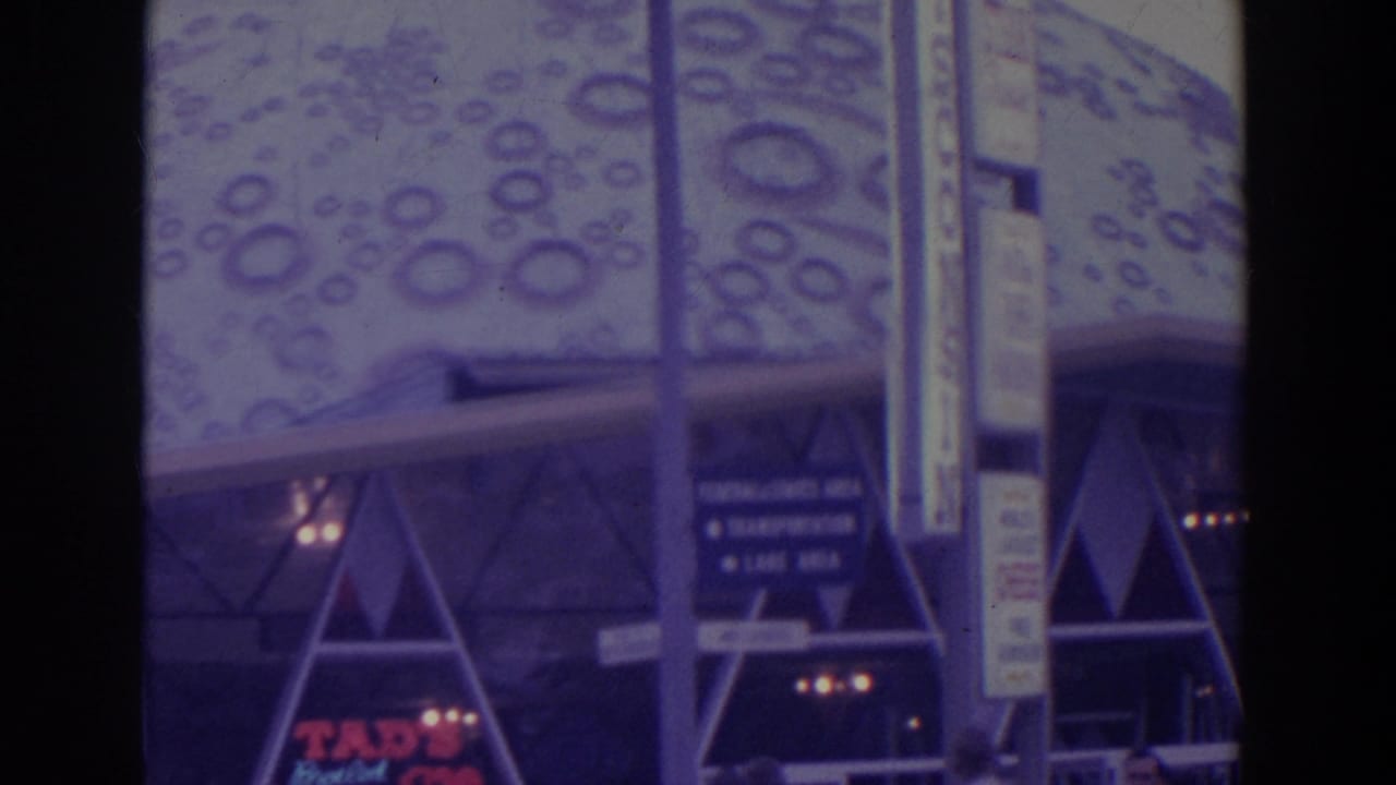 A patterned dome-like fair structure appears above directional signage, with pedestrians partly visible at street level.