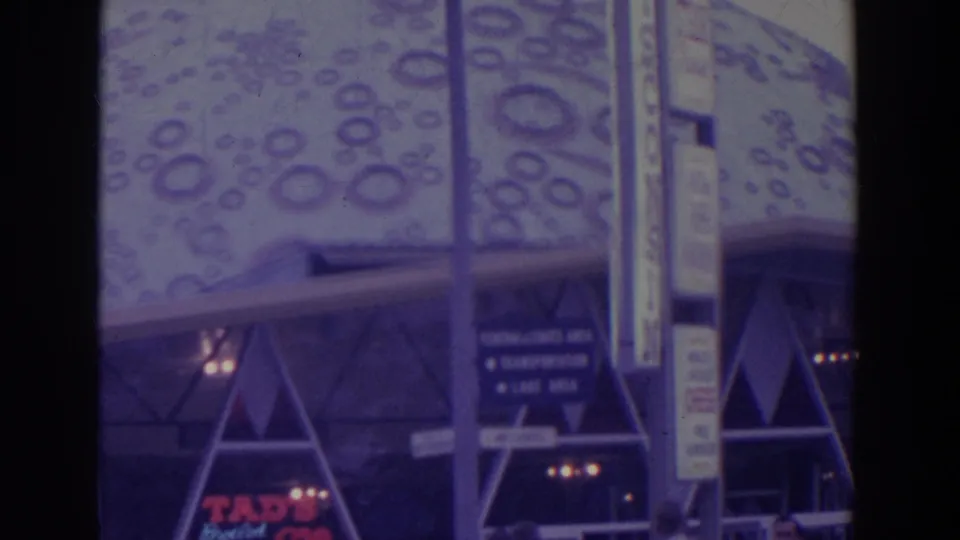 A patterned dome-like fair structure appears above directional signage, with pedestrians partly visible at street level.