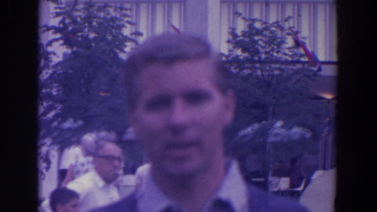 Man close to camera with other visitors and fair structures behind him.