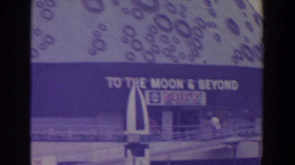 Fairground attraction facade with the visible words To the Moon & Beyond, railings, and visitors near the entrance.