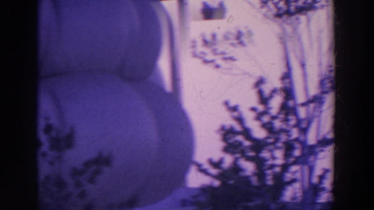 1964 8mm frame showing a purple-tinted upward view of trees, tower supports, and a dark partial structure at the edge.