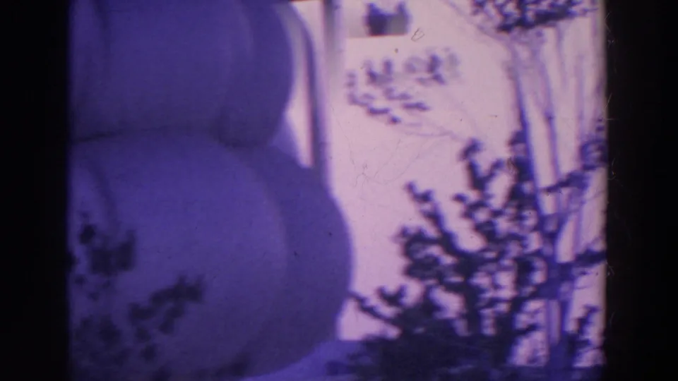 1964 8mm frame showing a purple-tinted upward view of trees, tower supports, and a dark partial structure at the edge.